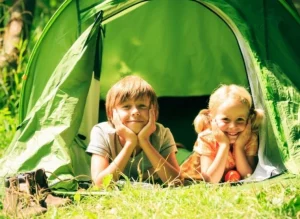Niños felices haciendo camping. Están en la carpa y miren al jardín.