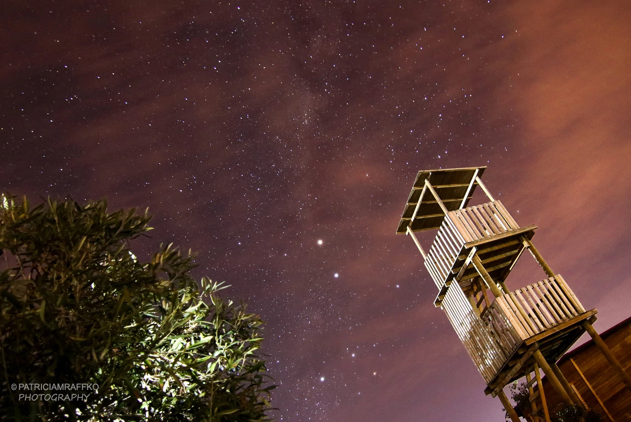 Cielo nocturno con estrellas y galaxias. Se ve la torre mirador de Ocho Águilas Eco Lodge.
