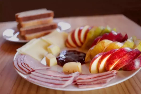 Desayuno saludable: Plato con jamón, queso y mantequilla. Diferentes frutas y verduras.