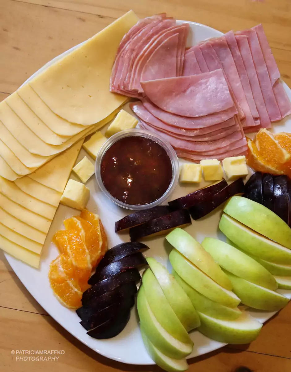 Desayuno tipo americano con un plato de frutas cortadas, jamón, queso, pan y mantequilla